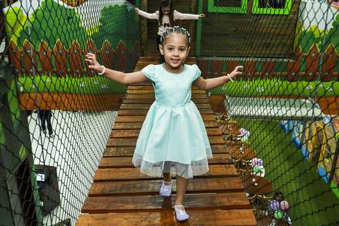 Fotógrafo de aniversário infantil na Vila Maria registra a aniversariante Melissa atravessando a ponte de madeira no Buffet Magia Kids Prime.'
