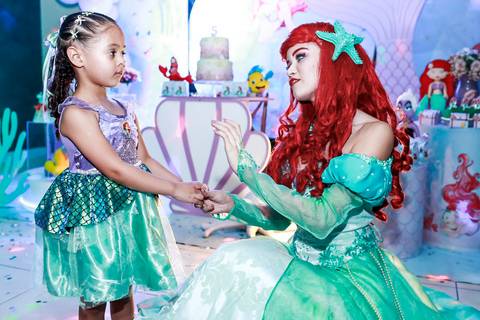 Fotografia de festa infantil na Vila Maria, com a aniversariante Melissa, fantasiada de Pequena Sereia, interagindo com a personagem Ariel.'