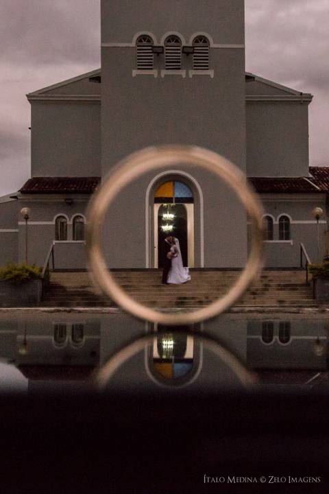 Fotografia dos noivos dentro da aliança em frente a igreja da matriz, durante ensaio fotográfico pós casamento realizado na cidade de Araçuaí, Minas Gerais'