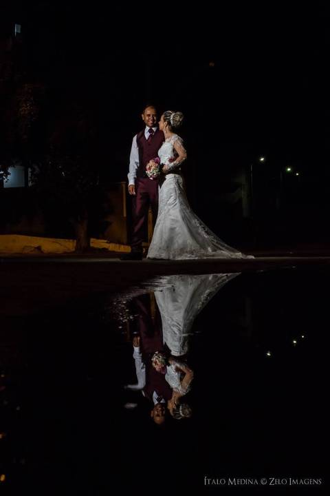 Foto simétrica dos noivos refletidos em uma poça de água em ensaio fotográfico pós casamento feito na cidade de Araçuaí - MG'