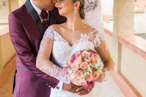 Fotografia dos noivos abraçados, com o narizes se tocando, enquanto a noiva segura o buquê'