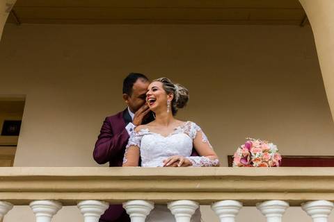 Fotografia do noivo falando algo no ouvido da noiva e ela sorrindo, durante ensaio fotográfico pós casamento realizado na cidade de Araçuaí, Minas Gerais'