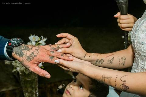 Fotografia de criança olhando enquanto a noiva coloca a aliança no dedo do noivo, ambos tatuados, durante casamento realizado em Coronel Murta - MG'