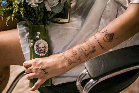 foto do braço da noiva, tatuado, segurando o buquê de flores com um pequena fotografia de sua avó, em making of de casamento realizado na cidade de Coronel Murta, Minas Gerais.'