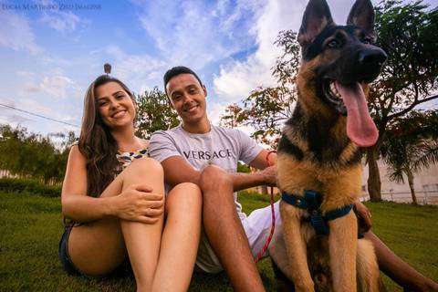 fotografia do casal sentado na grama, sorrindo com seu cachorro da raça pastor alemão, com a língua pra fora durante ensaio fotográfico pós casamento em Virgem da Lapa, Minas Gerais.'