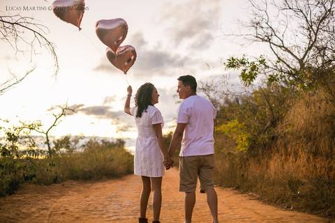 fotografia de casal com balões de coração em estrada de terra, durante ensaio fotográfico de casal.'