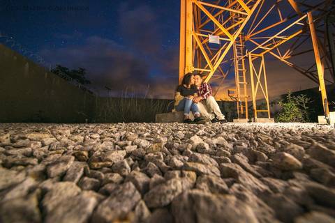 fotografia de casal sentado em base de uma torre de comunicação à noite, durante ensaio fotográfico de casal em Araçuaí, Minas Gerais'