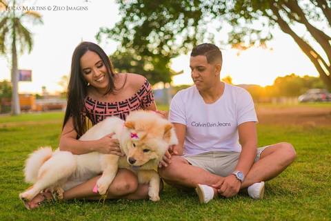 Casal sentado em gramado brincado com seu cão da raça Chau Chau durante por do sol em ensaio fotográfico feito na cidade de Araçuaí, Minas Gerais'
