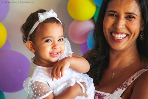 mão segurando a filha sorrindo com balões ao redor'