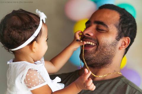 Filha brincando com o colar do pai no colo'