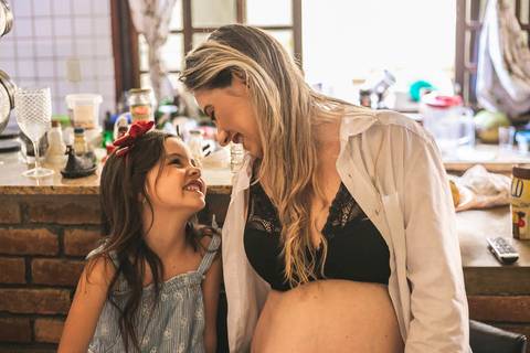gestante posando com sua filha na cozinha da casa com bancada de tijolinhos'