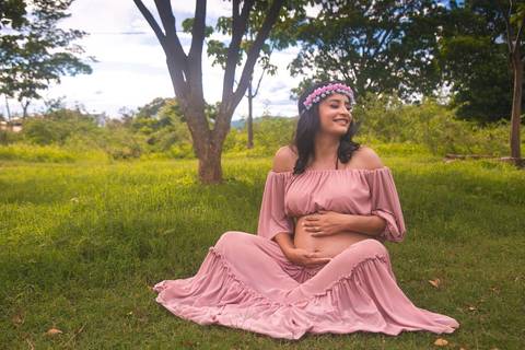 Gestante posando em um gramado verde com um vestido rosa e uma coroa de flores'