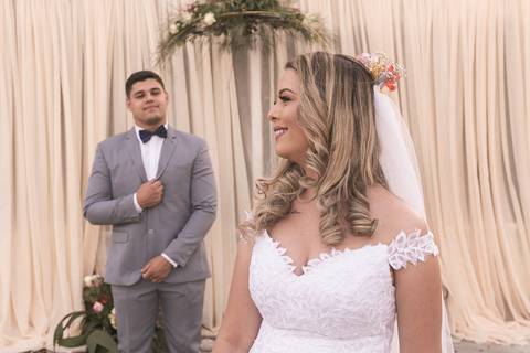 Casal vestindo terno e vestido de casamento posando à pouca distância.'