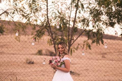 Noiva segurando seu buquê de flores cor de rosa em frente à uma tela enfeitada com lâmpadas.'