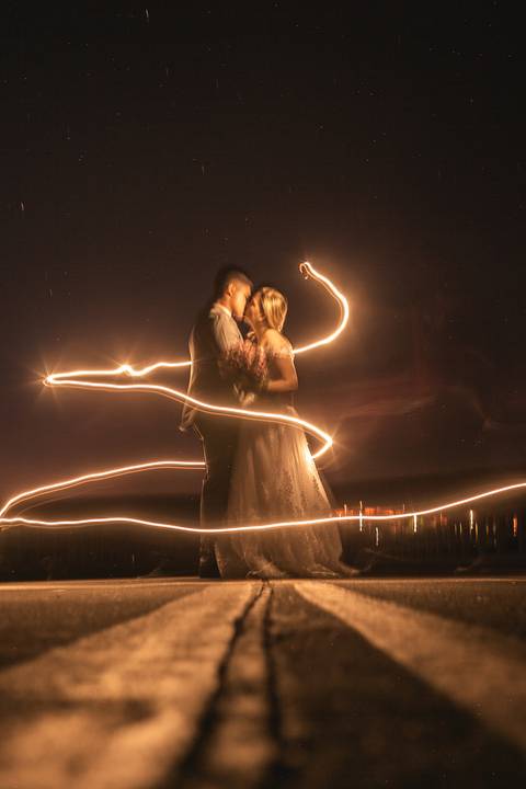 Casal vestindo terno e vestido de casamento, em foto noturna envoltos em feixe de luz'