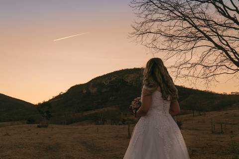 Noiva de costa observando o céu enquanto passa um avião à jato.'