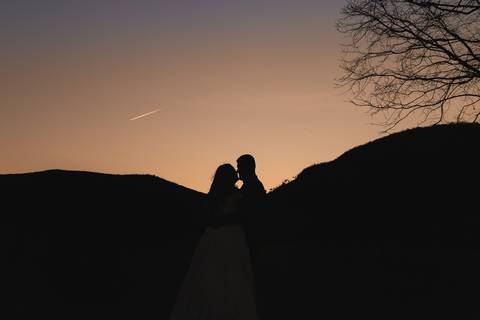 Silhueta de casal abraçados enquanto avistam um avião à jato no céu.'