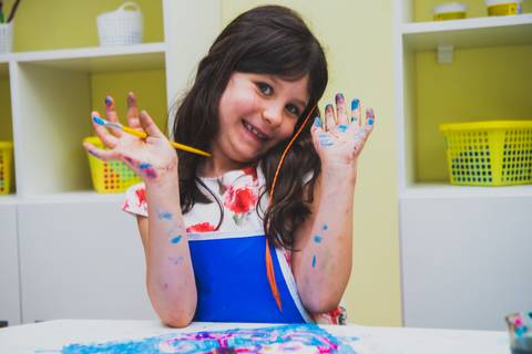 As mãos e cara suja de tinta desmonstram o quanto a menina está se divertindo'