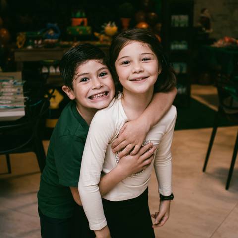 Aniversariante abraça irmã e posa para foto em frente a mesa de bolo'