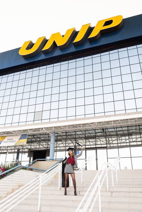 Foto com formanda em Direito na fachada da Universidade UNIP'