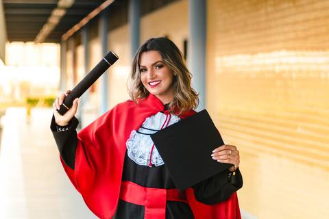 Formanda em Direito com faixa vermelha e capelo.'