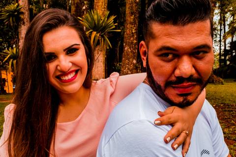 Ensaio pré-wedding, de um casal. Na foto temos um casal, sendo um homem e uma mulher, onde os dois estão sentados um ao lado do outro, sendo que, a moça está com a mão esquerda passando pelo ombro do esquerdo do rapaz e chegando no direito.'