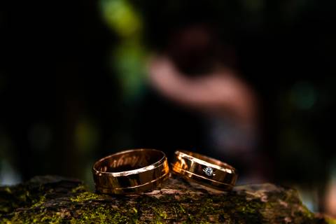 Foto de casal em ensaio pré wedding. O casal está ao fundo da foto totalmente desfocado, enquanto as alianças estão em sua frente em cima de uma pedra com todo o foco.'