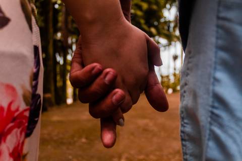 Casal caminhado de mãos dadas. A
foto está em close nas mãos.'