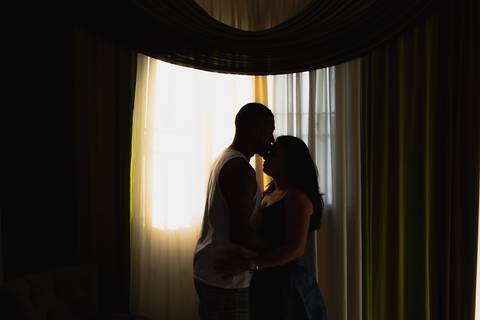 silhueta homem e mulher, homem beijando testa da mulher, na frente de uma janela
'