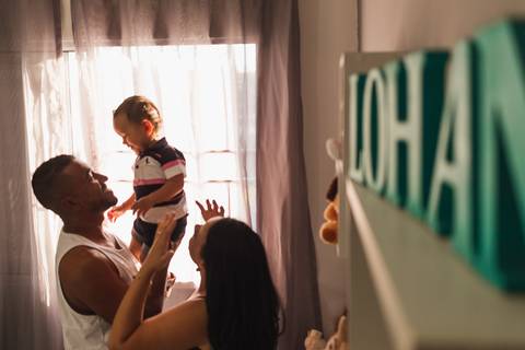 família brincando no quarto do bebê. O pai levanta a criança '