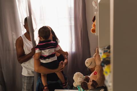 família brincando no quarto do bebê, o pai está se escondendo atrás da cortina '