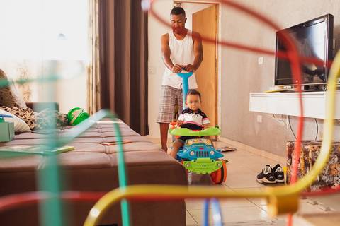 pai brincando com filho pequeno na sala, ele está empurrando a criança em um carrinho '