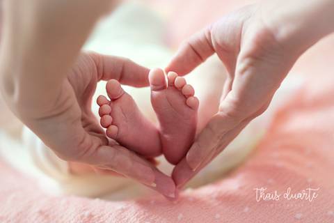 Mãe fazendo coração com as mãos enquanto segura pezinhos da bebê'