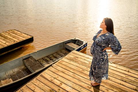 gestante posando para foto em ensaio com lago no fundo e um barco ao lado de vestido azul'