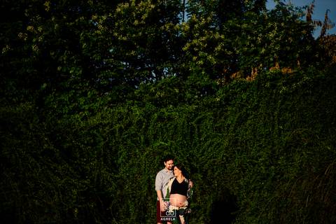 casal em ensaio de gestação ao ar livre com fundo verde de folhagens'