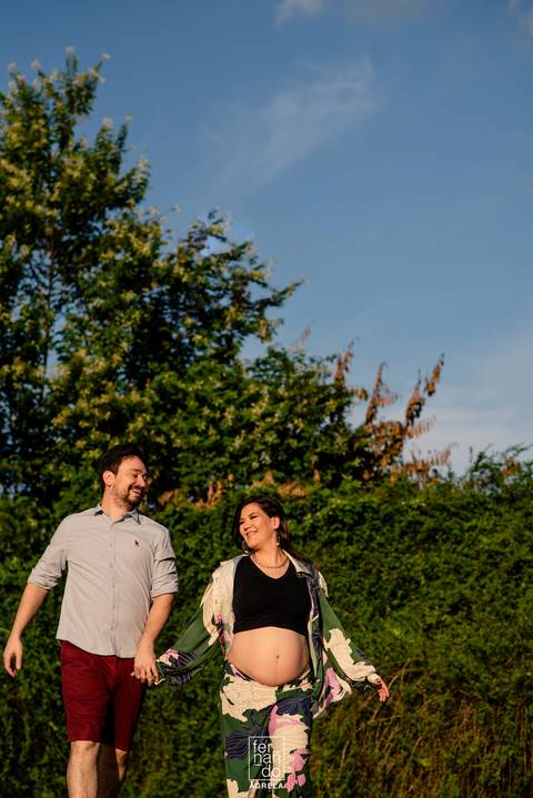 casal gestante caminhando em local aberto com fundo de vegetação'