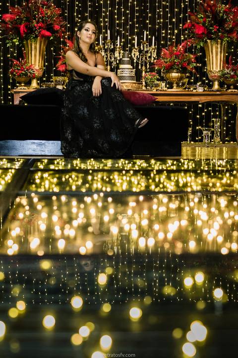 debutante sentada vestido preto pista led e mesa de bolo ao fundo'