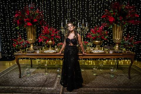 debutante sentada vestido preto pista led e mesa de bolo ao fundo'