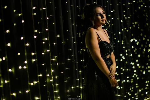 debutante sentada vestido preto pista led e mesa de bolo ao fundo'