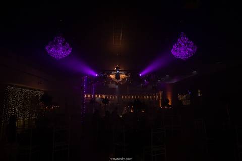 debutante sentada vestido preto pista led e mesa de bolo ao fundo detalhe dos lustres'