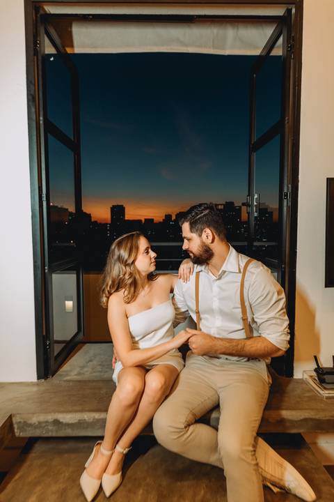 casal bem juntinho com cidade ao entardecer ao fundo'