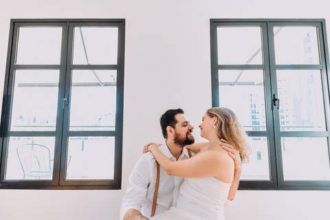 noiva sentada no colo do noivo com duas janelas grandes ao centro'