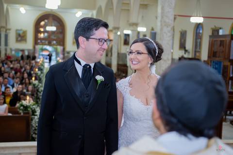 noiva e noivo trocando olhares no altar com padre de frente p/ eles'
