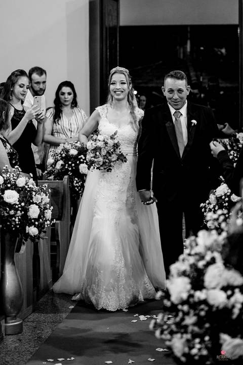 noiva entrando com pai e sorrindo preo e branco'