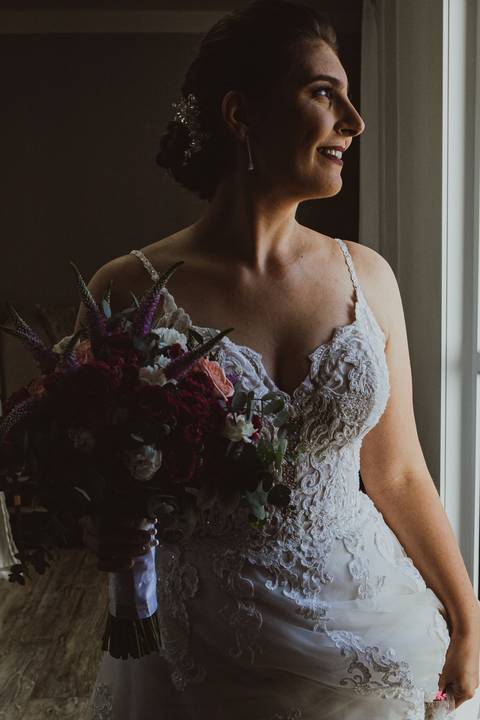 noiva com luz de janela e buque em mãos'
