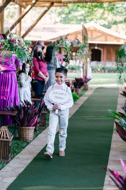 pajem com placa de la vem a noiva e sorrindo'