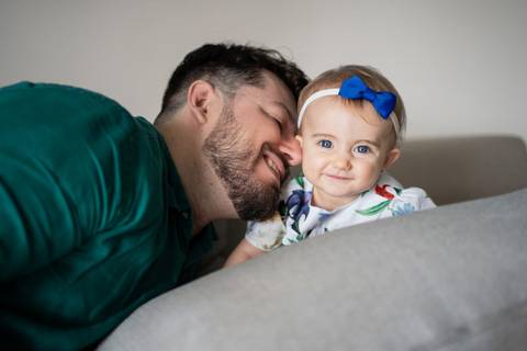 Bebê menina de 9 meses com lacinho azul na cabeça sorrindo para a câmera; pai sorrindo encostando o nariz e a testa na bebê; Joao-Francisco-Fotografia; Familia; Niteroi; Rio de Janeiro; Acompanhamento; life-style;'