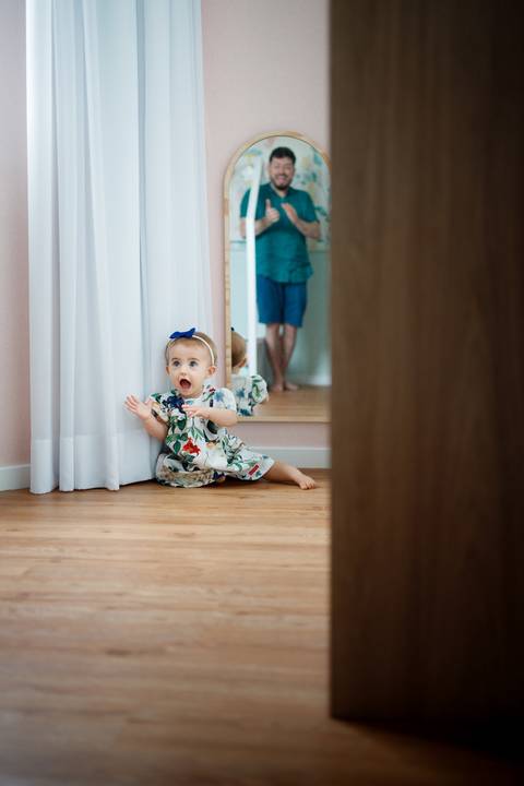 Bebê menina sentada no chão olhando pro pai que aparece batendo palmas refletido no espelho; Joao-Francisco-Fotografia; Familia; Niteroi; Rio de Janeiro; Acompanhamento; life-style;'