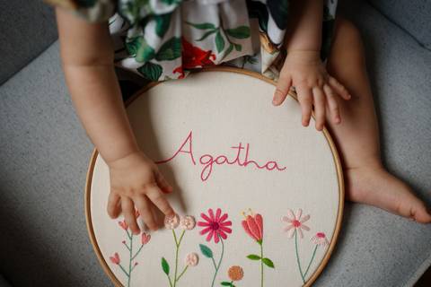 Detalhes dos braços e mãos de bebê segurando um bordado com o nome Agatha e desenho de flores; Joao-Francisco-Fotografia; Familia; Niteroi; Rio de Janeiro; Acompanhamento; life-style;'
