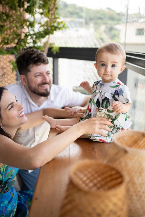 Pais agachados no chão admirando bebê sentada sobre a mesa; bebê olhando pra câmera; Joao-Francisco-Fotografia; Familia; Niteroi; Rio de Janeiro; Acompanhamento; life-style;'